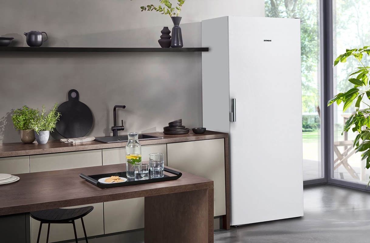 Hoge vrijstaande vriezer in een moderne keuken met donker aanrecht en grote raampartij