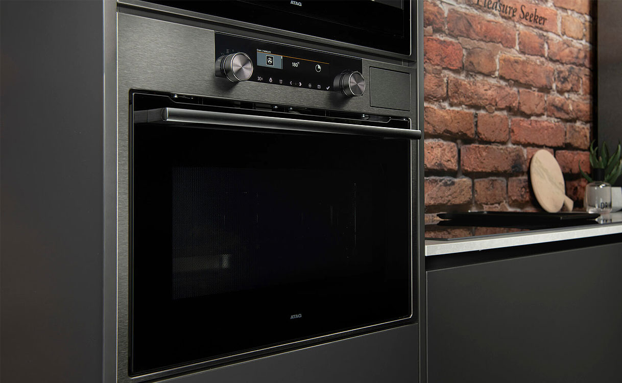 ATAG inbouw magnetron in donkere keuken met bakstenen muur en draaiknoppen voor nishoogte keuze
