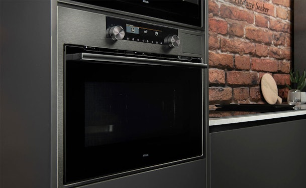 ATAG inbouw magnetron in donkere keuken met bakstenen muur en draaiknoppen voor nishoogte keuze
