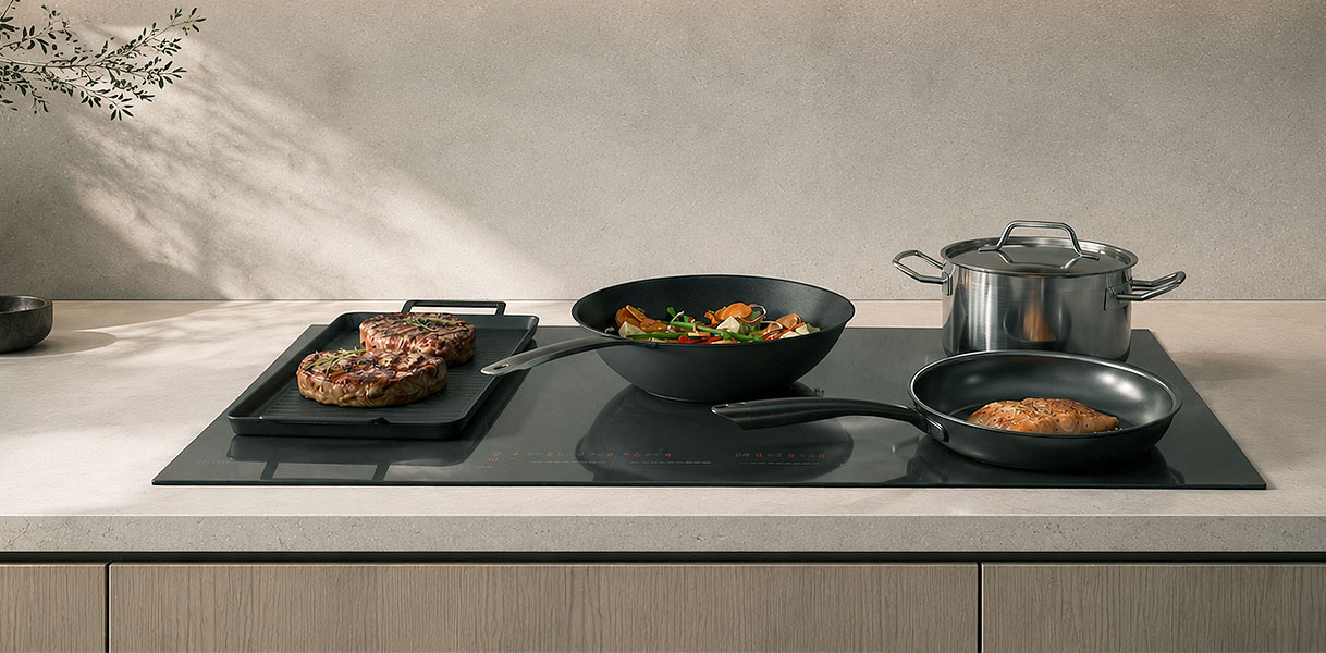 Grillplaat over twee gekoppelde zones naast een wok en een koekenpan op inductie