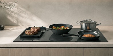 Grillplaat over twee gekoppelde zones naast een wok en een koekenpan op inductie