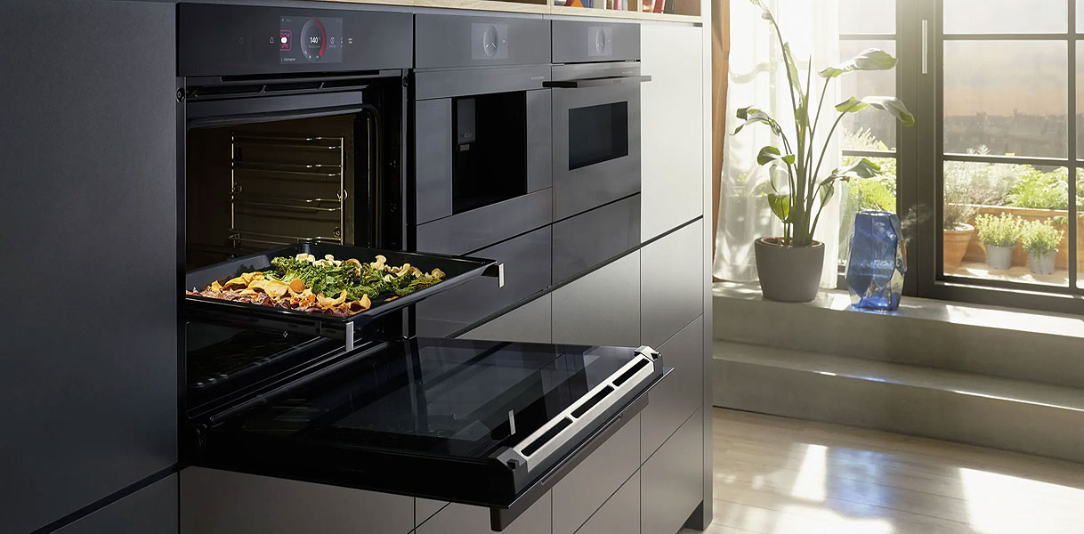 Inbouw magnetron met groenten op ovenrooster in moderne donkere keuken bij zonnig raam