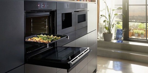 Inbouw magnetron met groenten op ovenrooster in moderne donkere keuken bij zonnig raam