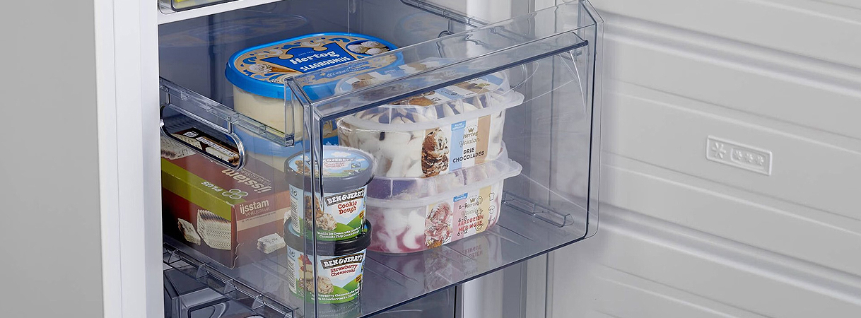 Gevulde transparante vriezerlade met ijs, brood en diepvriesproducten in een moderne vriezer