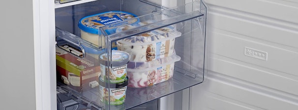 Gevulde transparante vriezerlade met ijs, brood en diepvriesproducten in een moderne vriezer