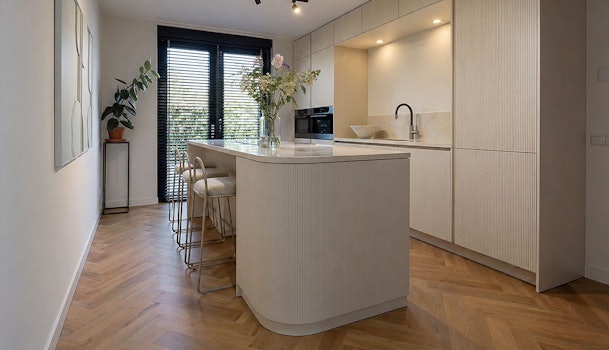 Smalle keuken met kookeiland tegenover kastenwand en lichte fronten in minimalistische opstelling