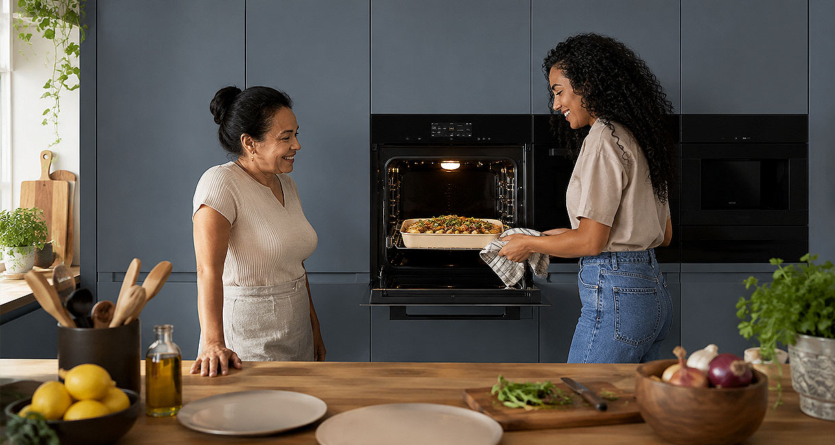 Twee vrouwen halen samen een grote ovenschotel uit de oven in een keuken