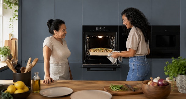 Twee vrouwen halen samen een grote ovenschotel uit de oven in een keuken