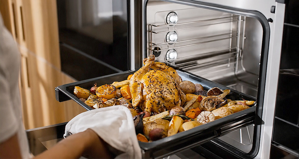 Braadslee met een hele kip en geroosterde groenten wordt uit de oven gehaald