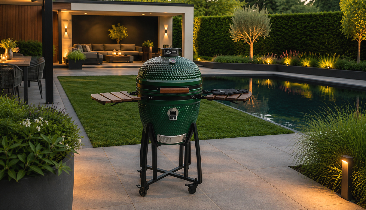 Groene kamado BBQ op een luxe terras bij een zwembad in een moderne tuin, geschikt voor grillen, roken en pizza bakken.