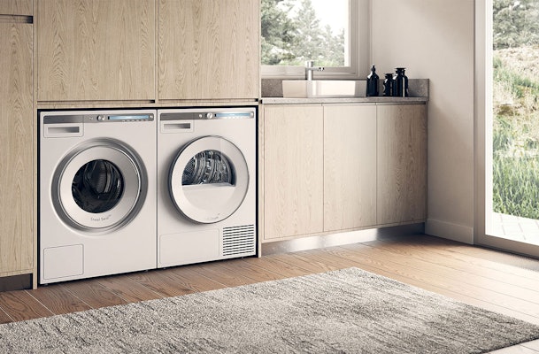 Asko wasmachine en droger geïntegreerd in lichte houten kastwand met moderne wasruimte