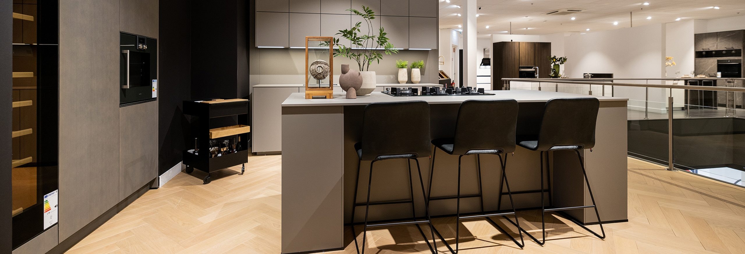 Minimalistische rechte keukenopstelling met kookeiland en hoge kastenwand in natuurlijke kleuren.