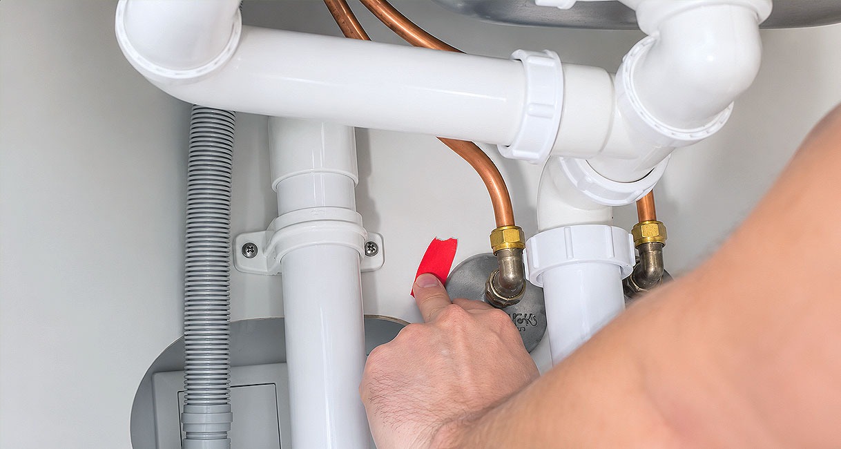 Hand plakt tape op de warmwaterleiding onder de spoelbak voordat de keukenkraan wordt vervangen