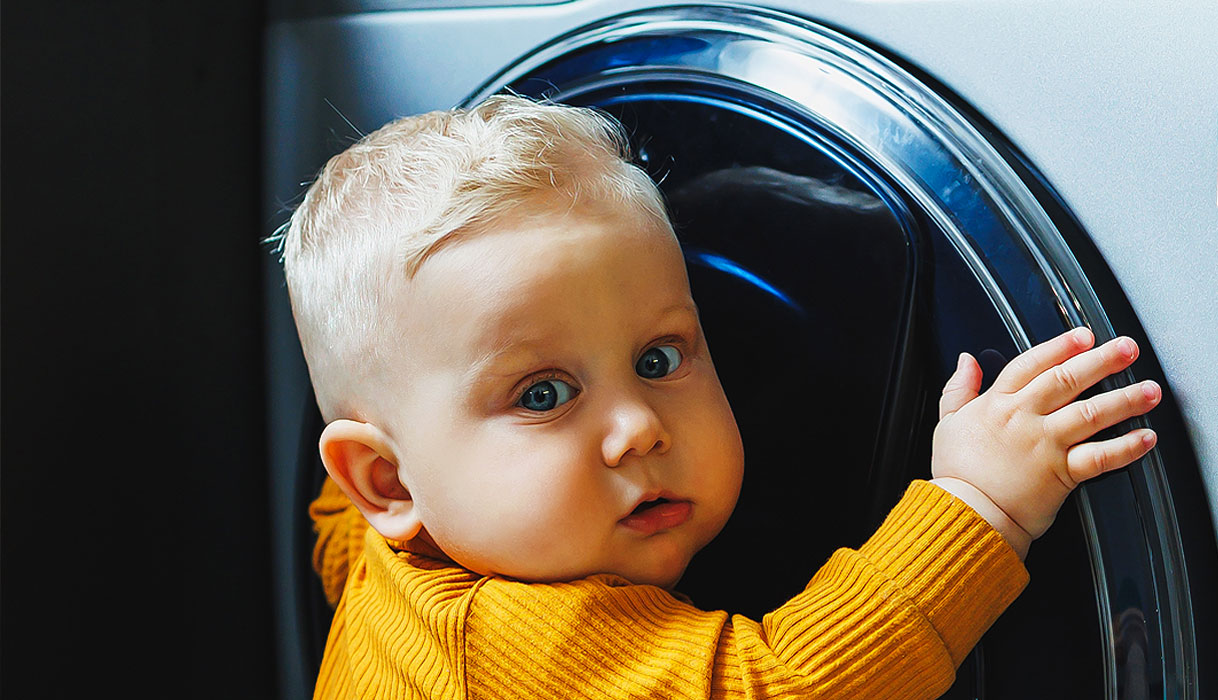 Peuter houdt zich vast aan de deur van een wasmachine