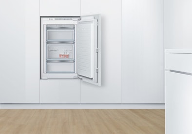 Kleine inbouw vriezer met drie lades, ingebouwd achter een keukendeur.