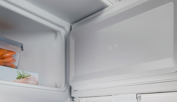 Compact vriesvak in een kleine inbouwkoelkast, met ingevroren producten op het bovenste schap.