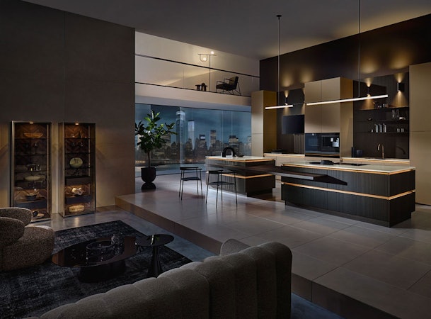 Luxe moderne keuken met donkere kasten, kookeiland en warme verlichting in open woonruimte.