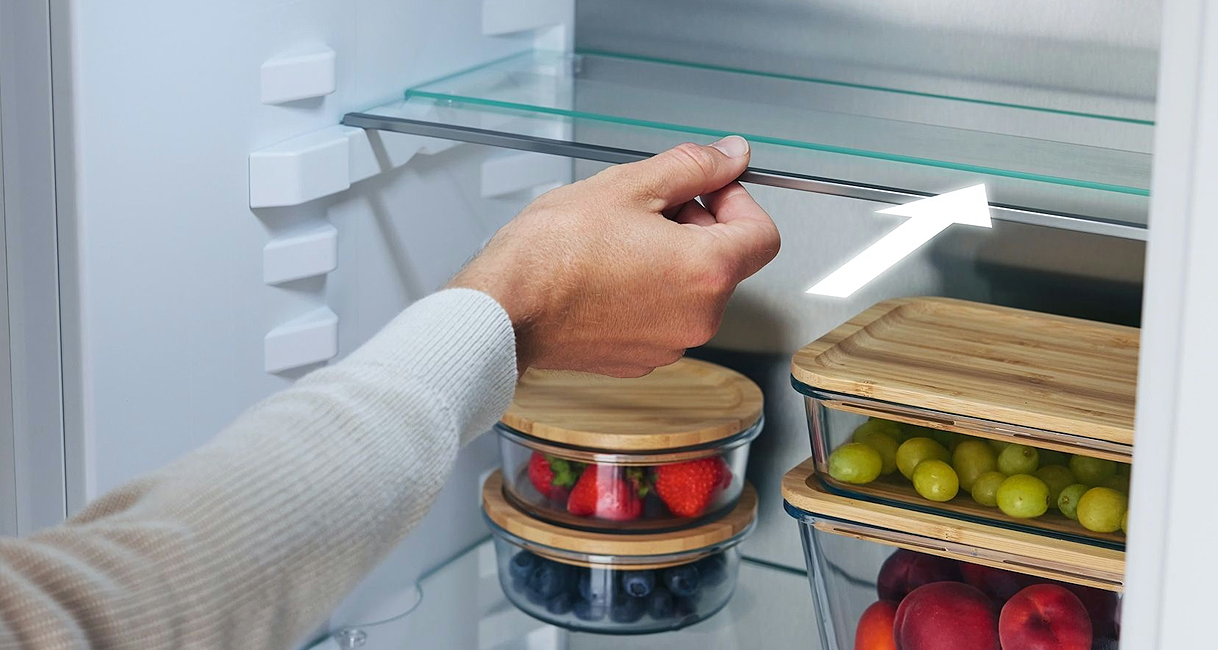 Hand die een glasplateau in een inbouwkoelkast verschuift om de indeling aan te passen.