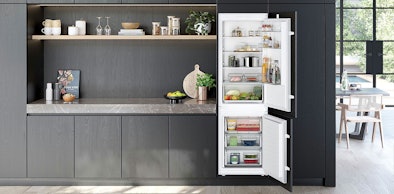 Volwaardige inbouw koel-vriescombinatie van 178 cm hoog in een moderne donkere keuken met open deuren.