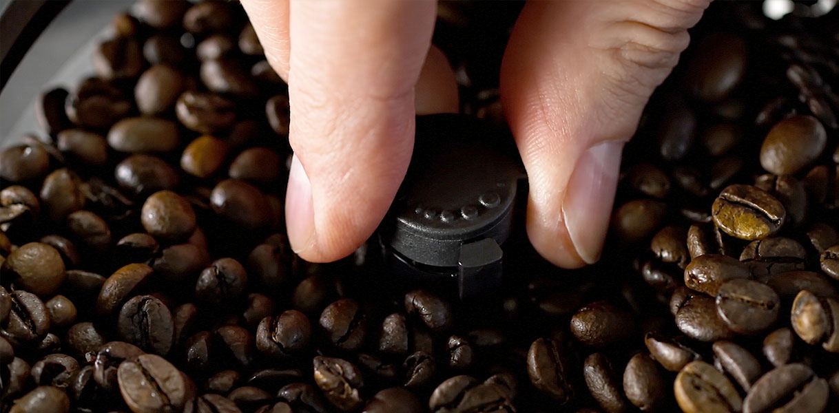 Hand die de maalgraad instelt op een koffiemachine met koffiebonen in het reservoir