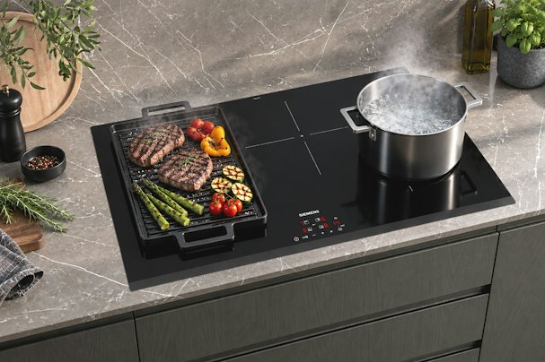 Inductie kookplaat met een grillplaat vol vlees en groenten naast een pan kokend water