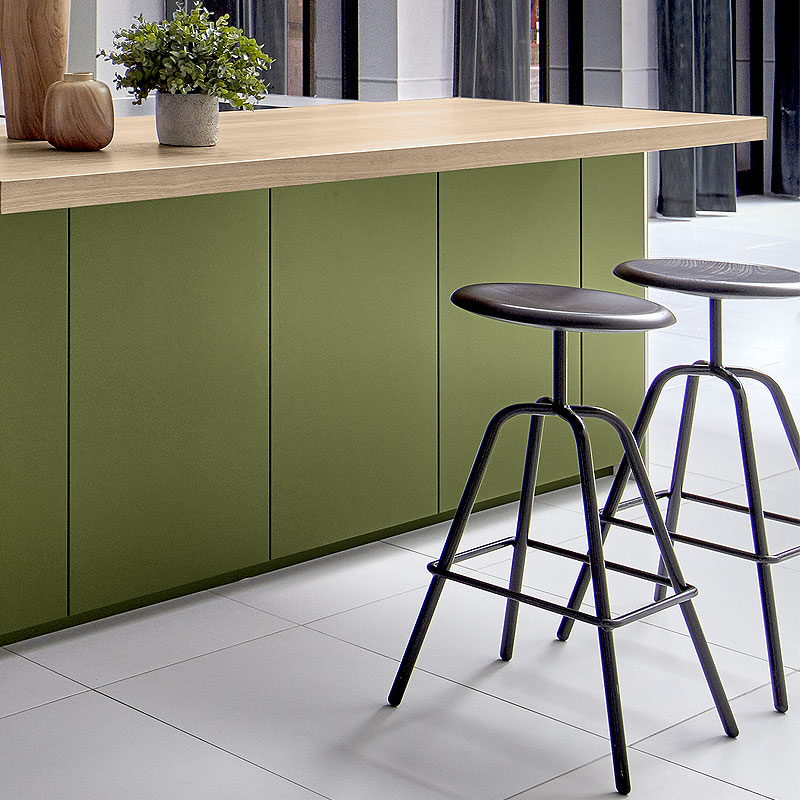 Kookeiland met verlengd houten werkblad, sepiagroene greeploze fronten en zwarte metalen barkrukken.