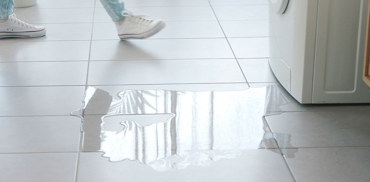 Plas water op de vloer naast een wasmachine