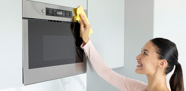 Vrouw die de buitenkant van een magnetron schoonmaakt met een zachte doek inclusief bedieningspaneel en deur