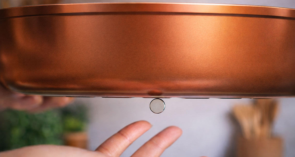 Hand houdt magneet tegen de koperen bodem van een pan om te testen op inductiegeschiktheid