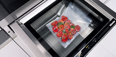 Vacuüm verpakte tomaten met kruiden op een plateau in een geopende stoomoven