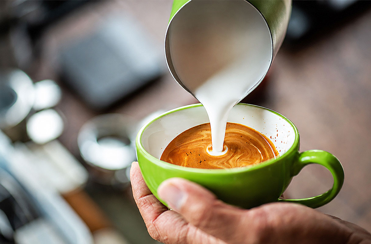 Opgeschuimde melk wordt vanuit een kannetje in een kop espresso geschonken voor een fijne schuimlaag