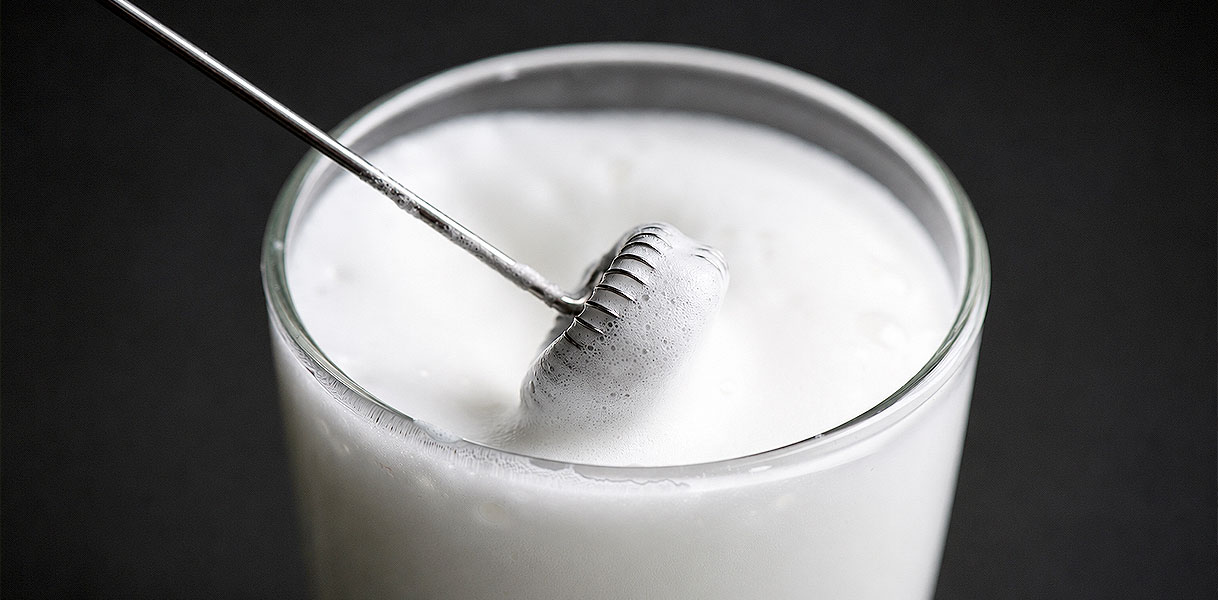 Garde van een melkopschuimer klopt de melk in een glas tot luchtig schuim