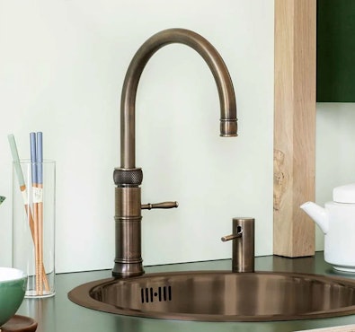 Quooker Classic Fusion kokendwaterkraan in messing patina finish boven een spoelbak, met zichtbaar warme bronzen kleur en verouderde uitstraling