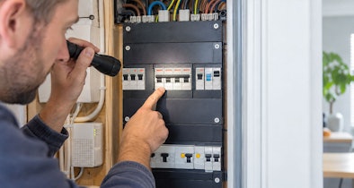 Man controleert met een zaklamp de gekoppelde automaten voor krachtstroom in de meterkast