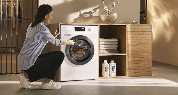 Vrouw plaatst was in een Miele wasmachine met 8 kg vulgewicht in moderne wasruimte.