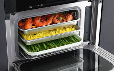 Combi-stoomoven met magnetron waarin garnalen, rijst en groene asperges gelijktijdig op meerdere niveaus worden bereid.
