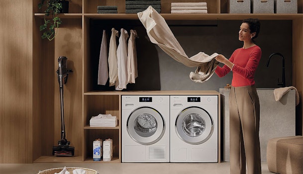 Vrouw vouwt wasgoed uit Miele wasdroger met DryCare 40 in moderne wasruimte
