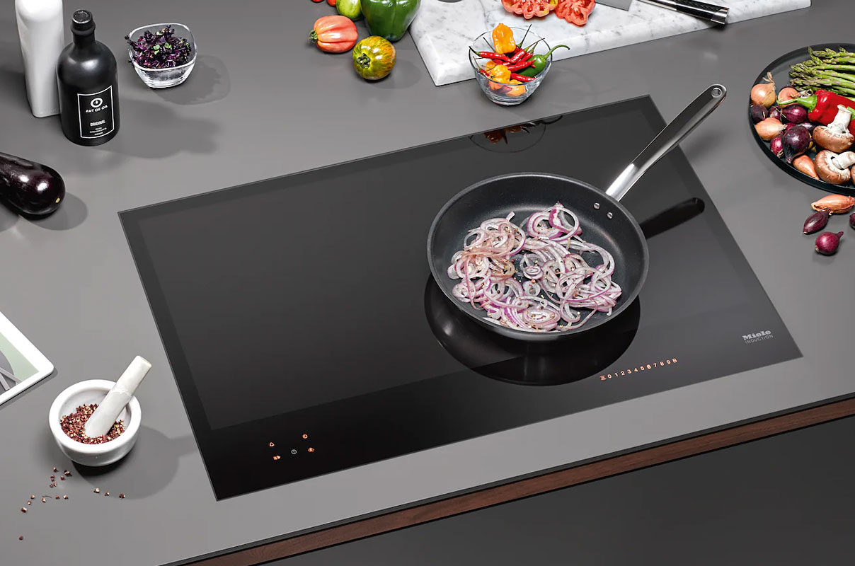 Miele inductiekookplaat met pan rode uien in moderne keuken met verse groenten