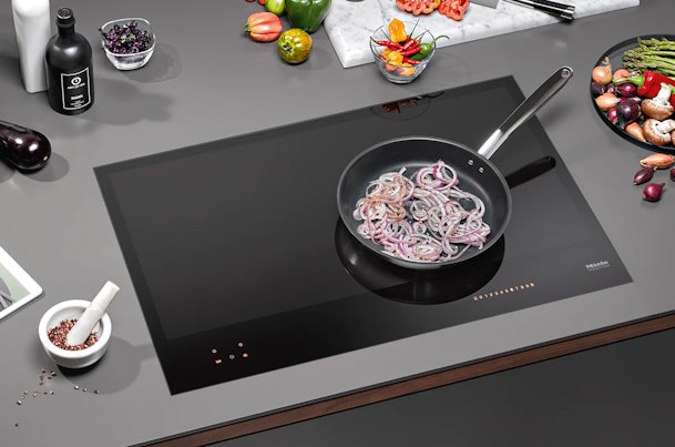 Miele inductiekookplaat met pan rode uien in moderne keuken met verse groenten