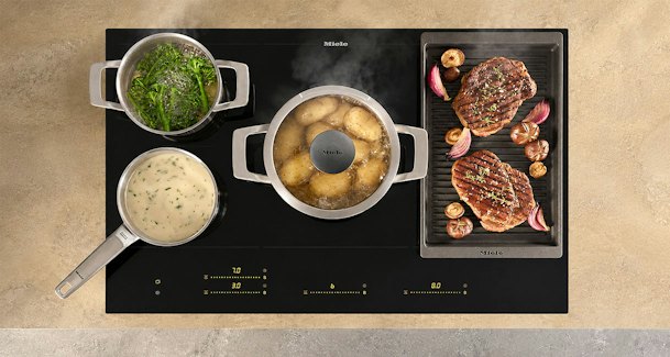 Inductiekookplaat met pannen op zones en grillplaat met steaks op gekoppeld PowerFlex vlak