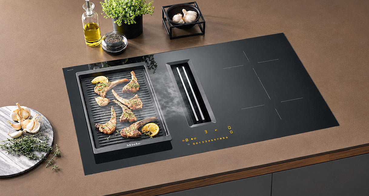 Inductie kookplaat met ingebouwde afzuiging die damp van grillplaat met lamskoteletten afvangt