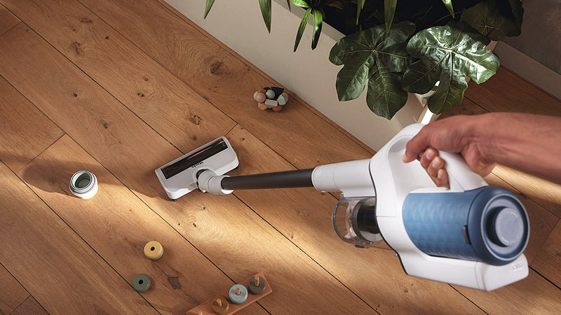 Miele snoerloze steelstofzuiger verwijdert vuil van houten vloer onder meubels