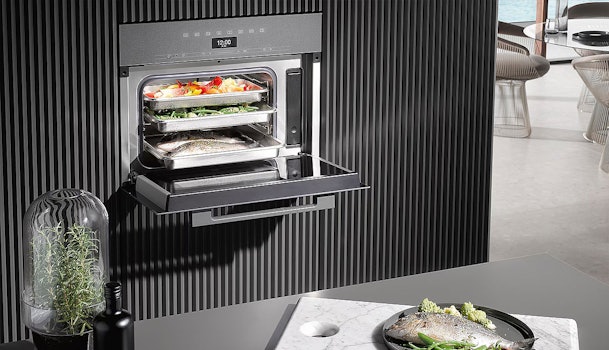 Geopende Miele stoomoven met verse gerechten op meerdere niveaus in een moderne keuken