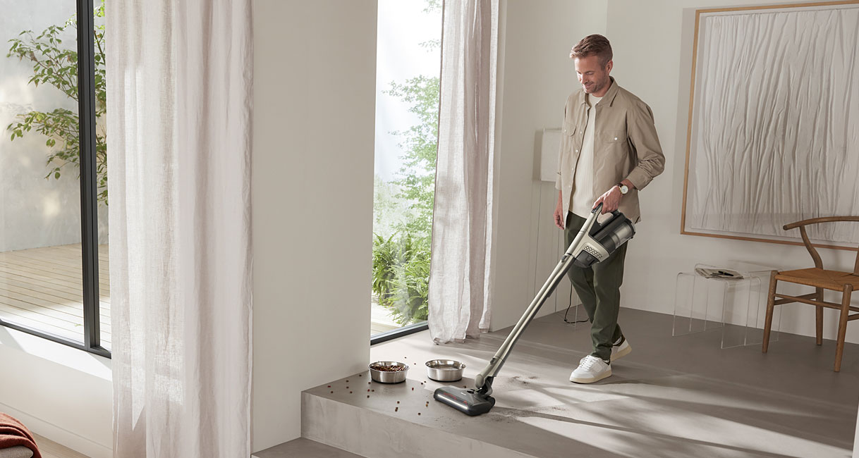 Man stofzuigt gemorst dierenvoer naast voerbakken met de Miele Triflex HX3 draadloze steelstofzuiger op een harde vloer