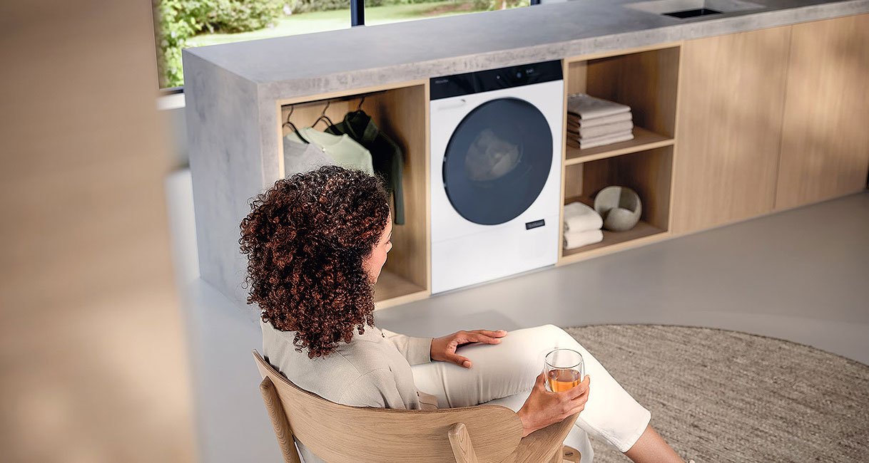 Vrouw ontspant voor Miele TQ serie warmtepompdroger Nova Excellence in moderne wasruimte