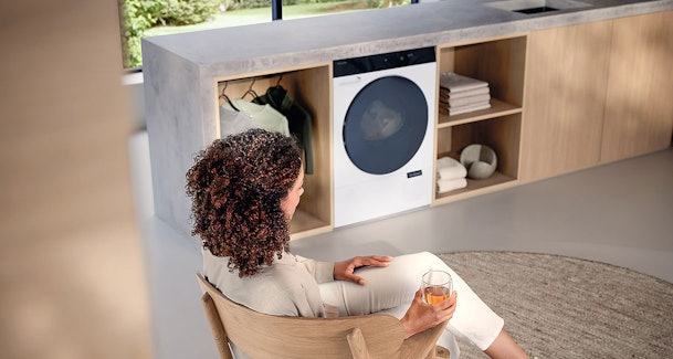 Vrouw ontspant voor Miele TQ serie warmtepompdroger Nova Excellence in moderne wasruimte