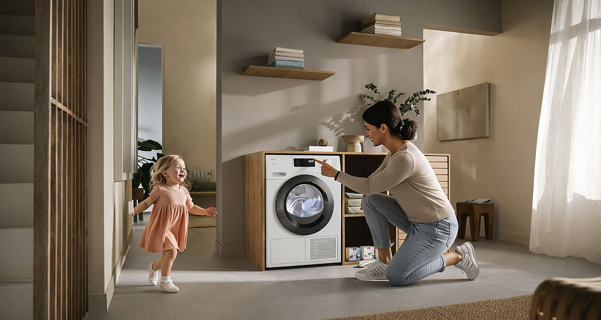 Vrouw met kind bedient Miele warmtepompdroger van 8 tot 9 kg in lichte wasruimte
