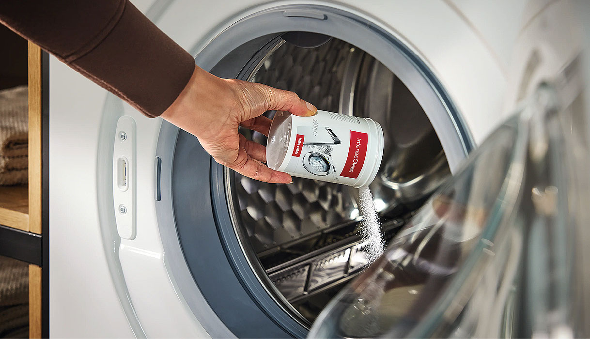 Hand die reinigingsmiddel in de trommel van een Miele wasmachine strooit