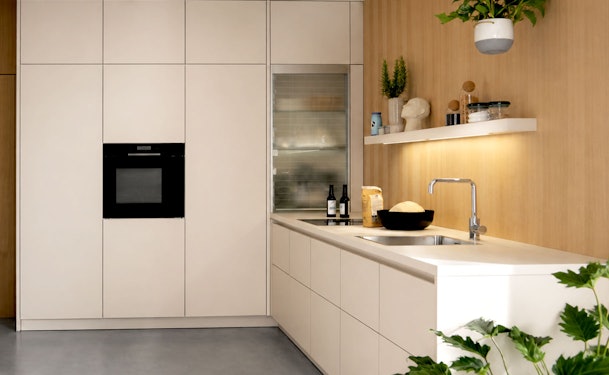 Moderne hoekkeuken met greeploze beige fronten, houten achterwand en wit keramisch werkblad