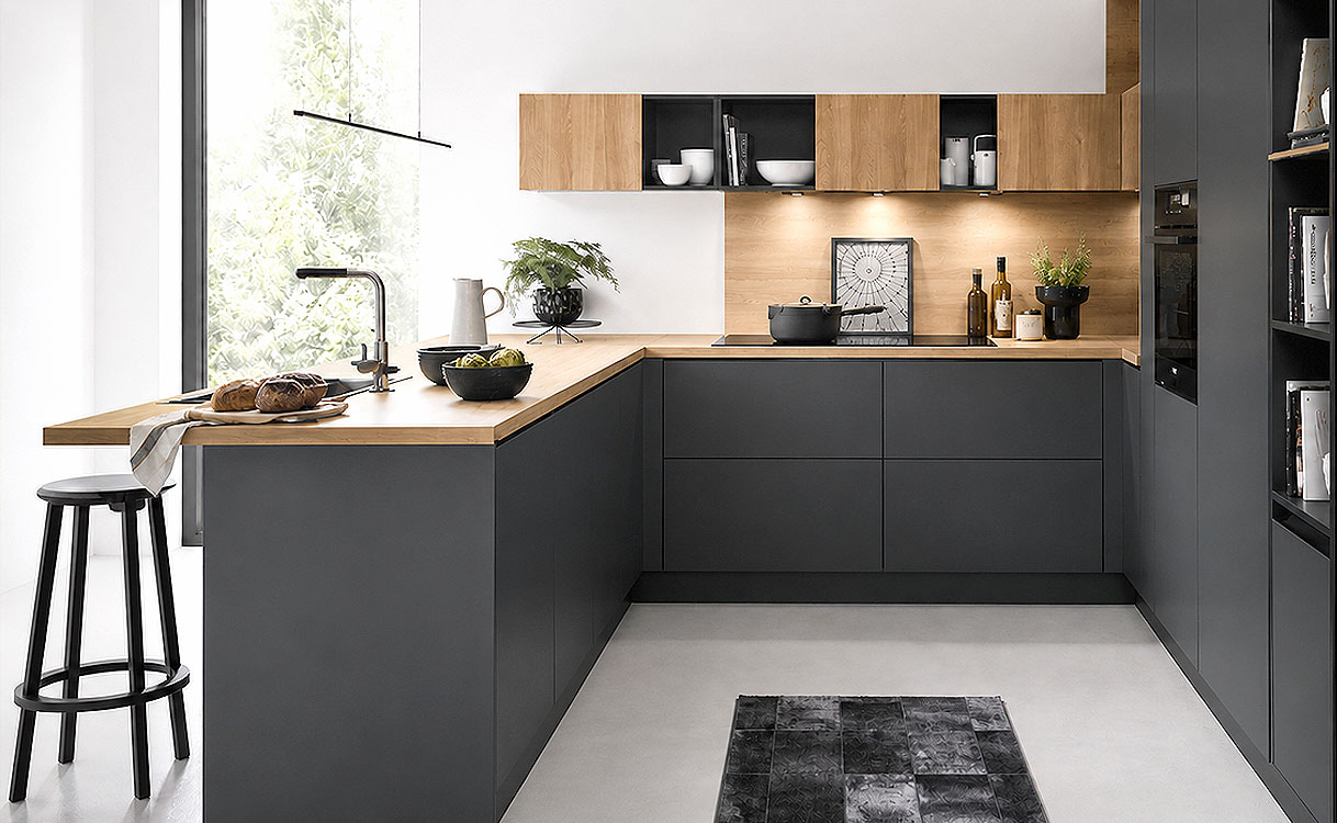 Moderne L-keuken met donkere greeploze fronten, houten werkblad en open woonkeukenopstelling